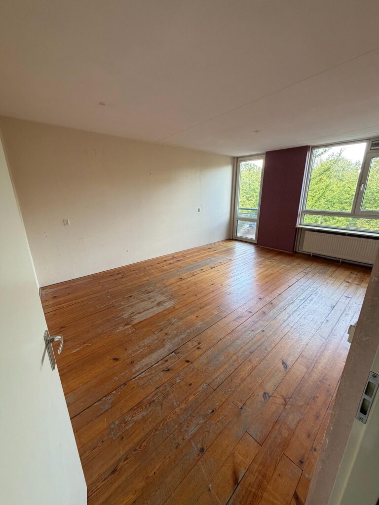 Dezelfde woonkamer leeg, met houten vloer en lege muren