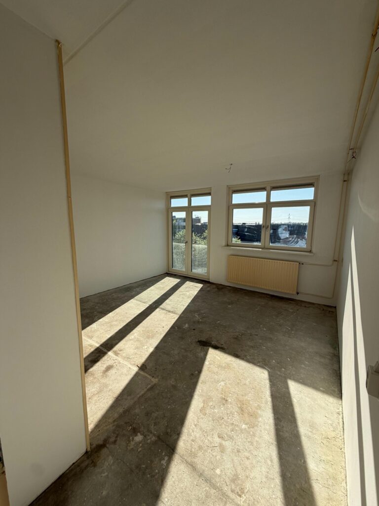Lege, opgeleverde kamer met kale vloer en licht door twee ramen