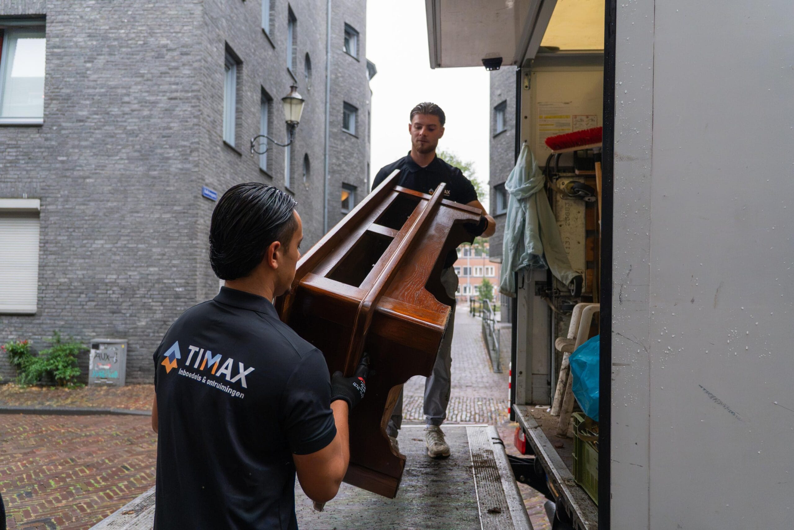 Medewerkers van Timax laden een houten kast in de verhuiswagen